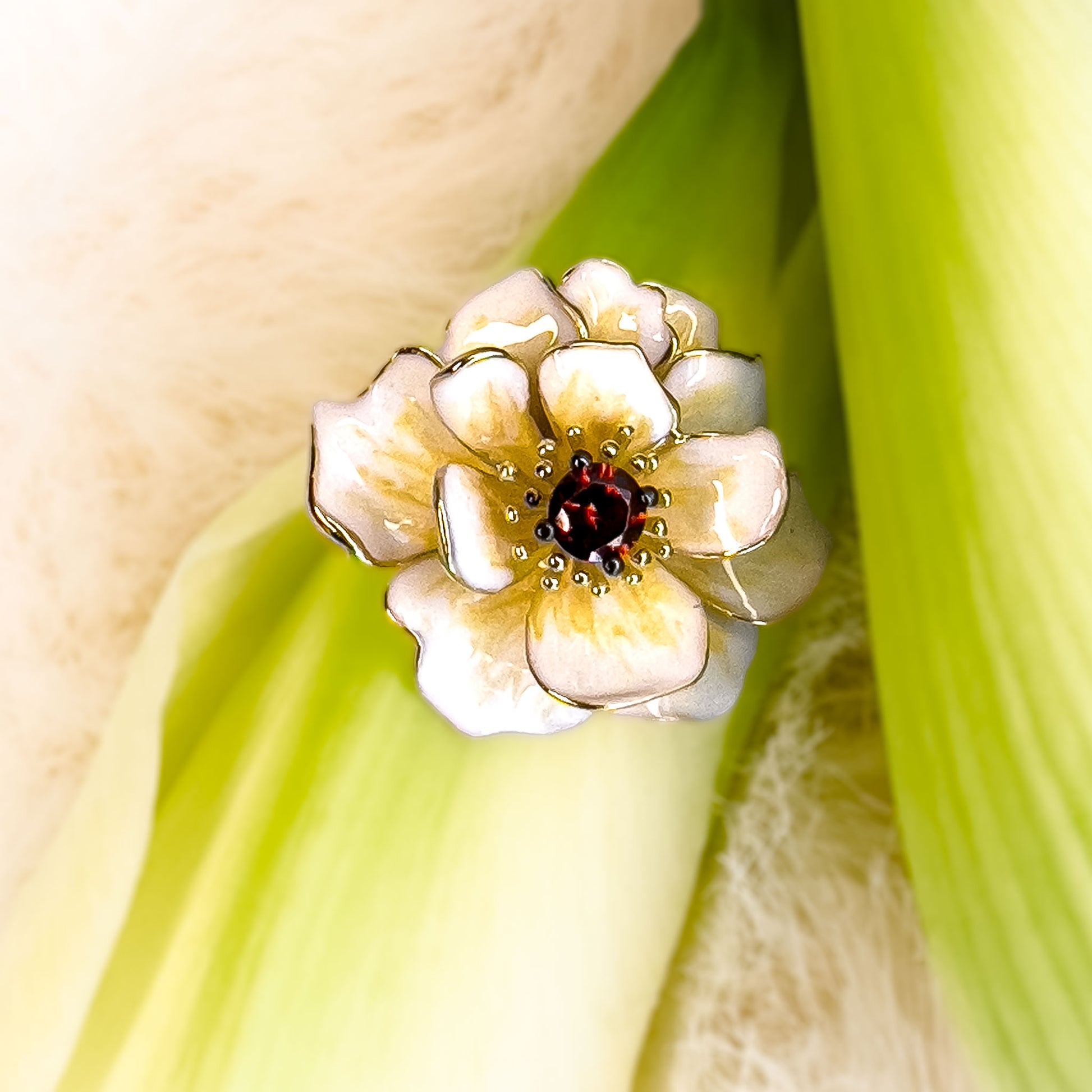 Sølv anheng i blomst forme med granat cubic zirkonia i midten av Hvit Magnolia Anheng, omgitt av delikate håndmalte emaljedetaljer. Et sølv smykke i gullbelagt sølv med emalke og stener.